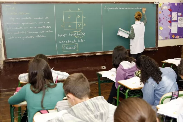 Sala de aula: professora passa matéria no quadro negro e alunos copiam