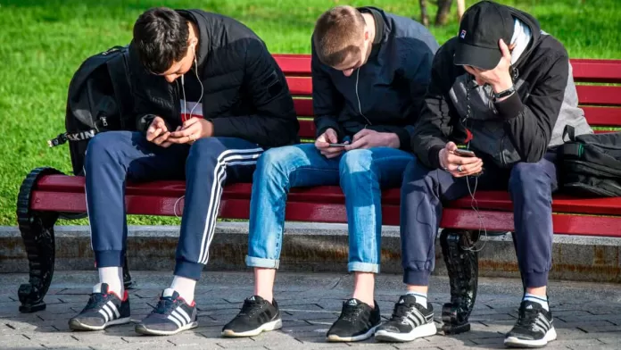 Três rapazes usando smartphone em banco de praça