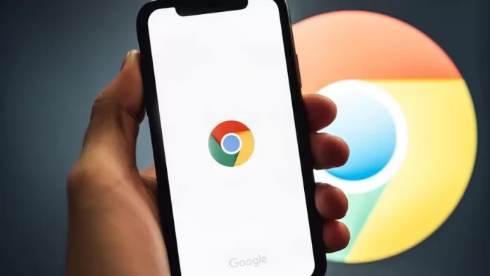 Pessoa segurando celular com logotipo do Google Chrome, também exibido em tela de computador ao fundo