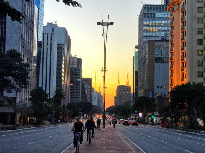 Pessoas andam de bicicleta ao entardecer numa avenida