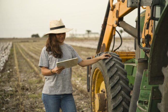 Retrato de agricultora jovem sorridente usando tábua e trator para colheita. Agricultura moderna com o conceito de tecnologia e máquinas