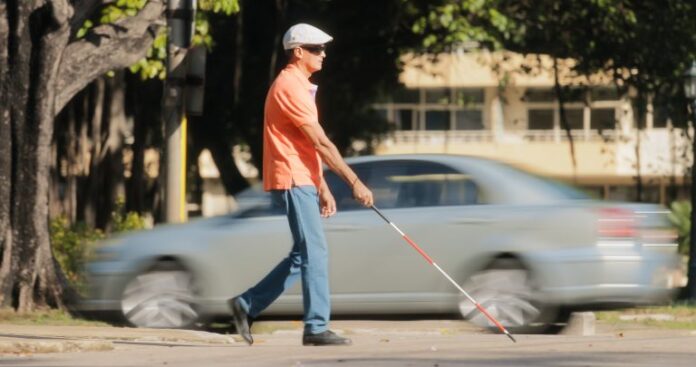 Um homem cego caminha com uma bengala pela rua