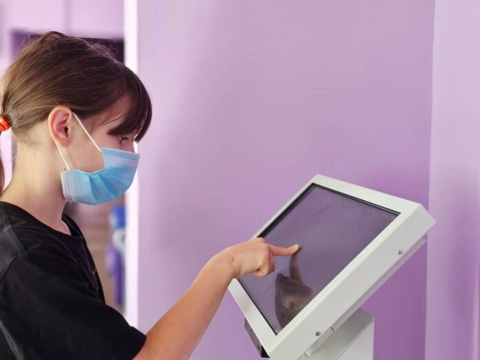 Imagem mostra uma mulher vestindo uma máscara cirúrgica tocando em uma tela digital em um hospital