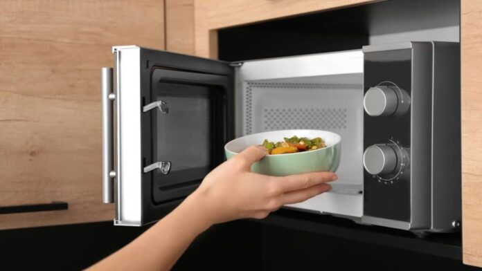 mãos de mulher colocando uma tigela com comida dentro do micro-ondas na cozinha