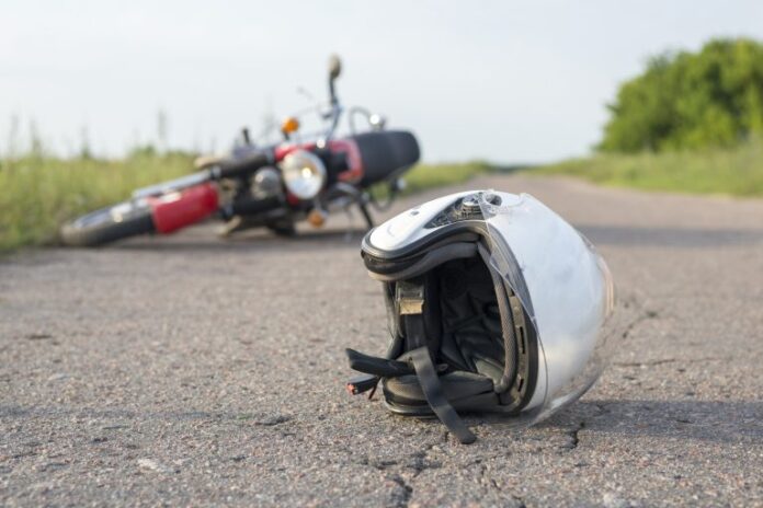 Uma moto caída no chão e em primeiro plano um capacete de motoqueiro