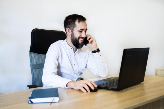 Homem sentado em uma cadeira, sobre a mesa há um notebook e uma agenda