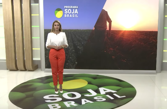 Apresentadora com camisa branca e calça laranja no estúdio do Soja Brasil