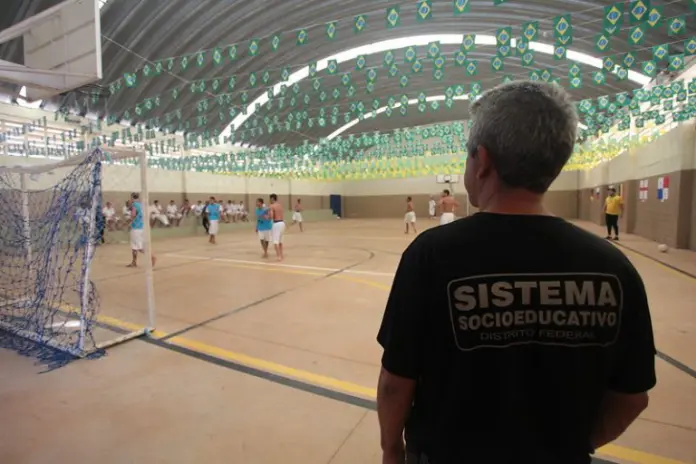 Agente socioeducativo observa adolescentes em conflito com a lei em quadra de esporte em Unidade de Internação no Distrito Federal